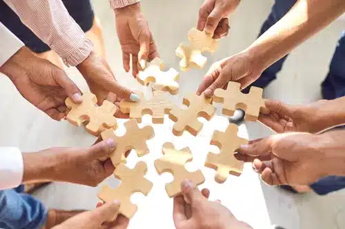 Close up of company workers finding solution in corporate work meeting. Cropped office employees learning to collaborate and playing with pieces of jigsaw puzzle during team building activity